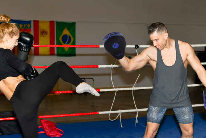 Woman delivering a high kick to a  AQF Boxing Focus pad held by a man